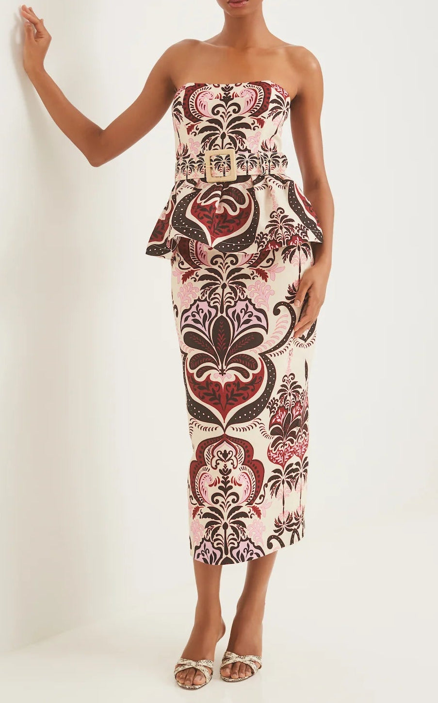 A woman wearing the Cara Cara Sienna Skirt, a bold pink, brown, and cream patterned midi with peplum waist, paired with a strapless fitted top and white heeled sandals.
