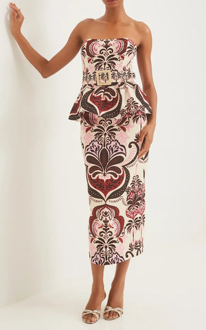 A woman wearing the Cara Cara Sienna Skirt, a bold pink, brown, and cream patterned midi with peplum waist, paired with a strapless fitted top and white heeled sandals.