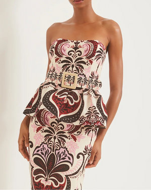 A woman wears the Cara Cara Tilda Top, a strapless peplum style featuring a bold, ornate pink and brown pattern with a matching wide belt and square buckle for added flair.