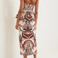 A woman faces away, wearing the Cara Cara Sienna Skirt, an ankle-length piece with a waisted fit and bold red, pink, and brown floral scroll patterns, styled with heeled sandals.