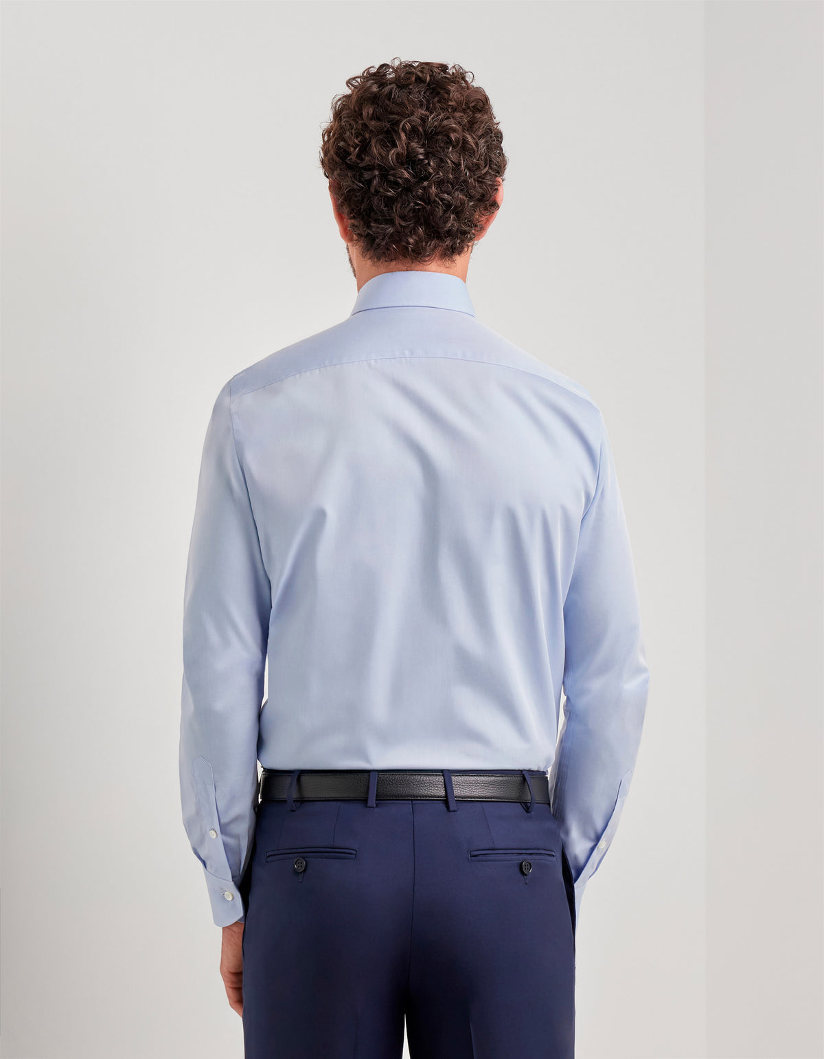 Rear view of a man wearing a light blue Canali Impeccabile Regular Fit Shirt tucked into navy blue trousers with a black belt.