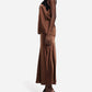A person stands in profile wearing CO's Slip Silk Skirt, a brown satin bias cut style, paired with a matching camisole featuring black lace trim and black high-heeled sandals.
