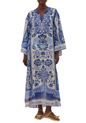 A person wearing the Farm Rio Delicate Tapestry Long Cover Up, featuring blue and white botanical patterns and wide sleeves, pairs it with brown sandals while standing against a white background.