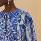 A person wearing the Farm Rio Delicate Tapestry Long Cover Up with botanical patterns and a tie neckline, styled with cream leaf-shaped earrings against an off-white beige background.