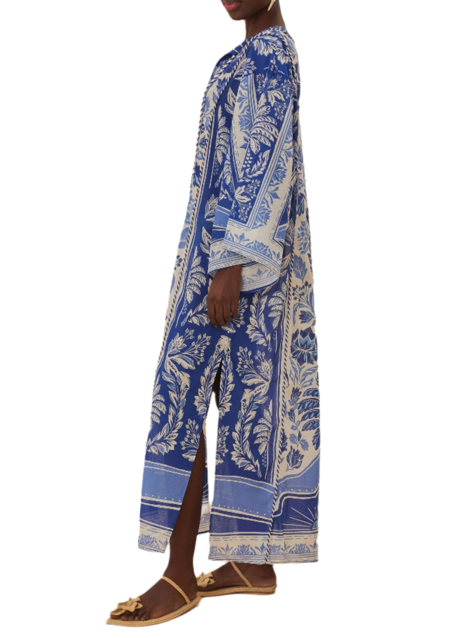 A person models the Farm Rio Delicate Tapestry Long Cover Up, a blue and white botanical-print kaftan with side slits, paired with flat sandals, standing against a white background.