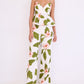 A woman stands against a plain background wearing Cara Cara’s Sunflower Pant, featuring a green and pink floral print, paired with a white sleeveless peplum top for a chic, tailored look.