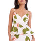 A woman wears the Avenue Top by Cara Cara, a white fitted peplum top with green leaf and pink flower print, adjustable straps, and a stylish peplum hem.