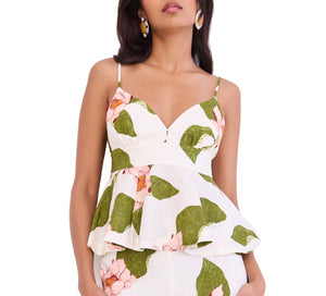 A woman wears the Avenue Top by Cara Cara, a white fitted peplum top with green leaf and pink flower print, adjustable straps, and a stylish peplum hem.