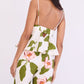 A woman is seen from the back wearing the Cara Cara Avenue Top—a white fitted peplum top with adjustable thin straps, a pink and green floral print, ruffled peplum hem, and a back cutout.