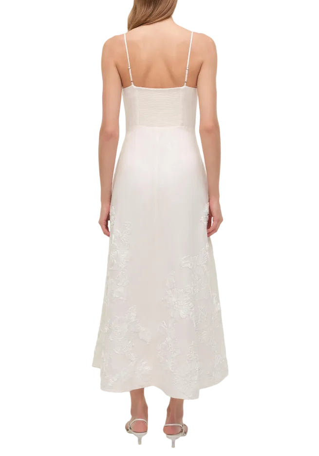 A woman in Simkhai's Annabella Soutache Dress—white, sleeveless, with thin straps and delicate embroidery—seen from the back and paired with heeled sandals.