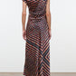 A woman stands with her back to the camera wearing the Staud Portia Silk Studio Dress, an off-shoulder, asymmetrical silk piece adorned with geometric and floral patterns, featuring an adjustable tie detail and paired with black shoes.