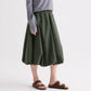 A person wears a grey long-sleeve top, brown sandals, and the TWP Full Intentions Superfine Cotton Skirt in green while standing against a plain background.