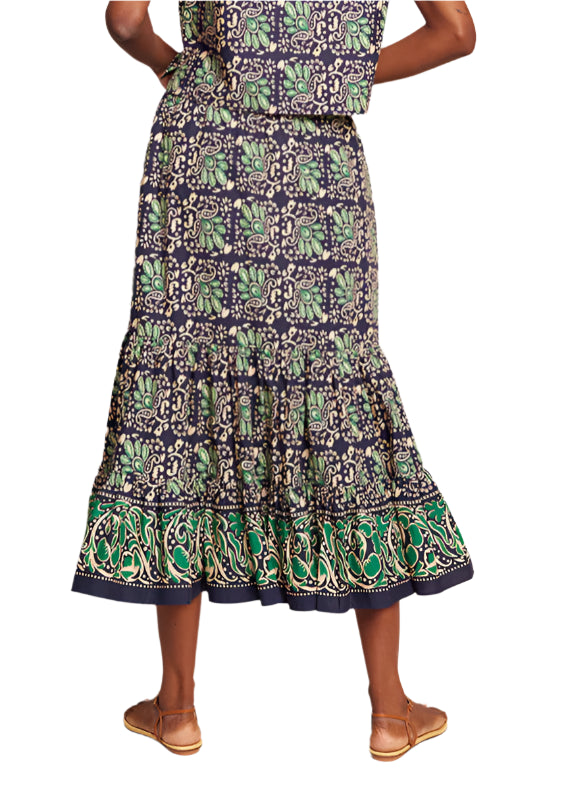 Wearing the Cara Cara Chase Skirt with an elastic waistband, a person enjoys comfort in this ankle-length cotton poplin garment adorned with green, navy, and beige designs. Perfectly paired with tan sandals.