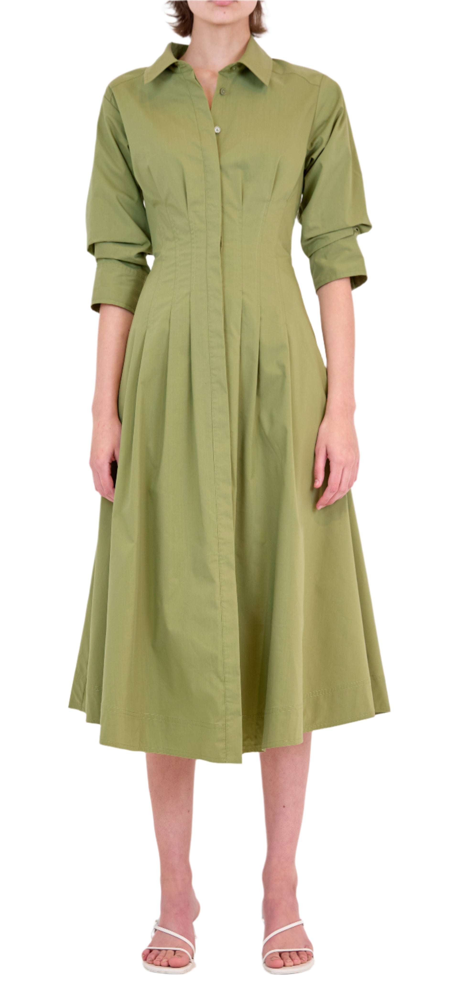 A woman wears the Simkhai Signature Jazz Dress, a light green, collared cotton poplin button-down midi with pleats and an A-line silhouette, paired with white heeled sandals.