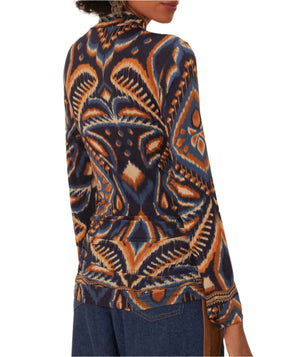 A person is wearing a Farm Rio Pineapple Ikat Blue Jersey Blouse, featuring a distinctive geometric print in shades of orange, blue, and black, paired effortlessly with blue jeans.