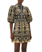 A person wearing a Farm Rio Ainika Tropical Splendor Blue Mini Dress featuring intricate floral and abstract tropical patterns, puffed sleeves, button details, and a high neckline.