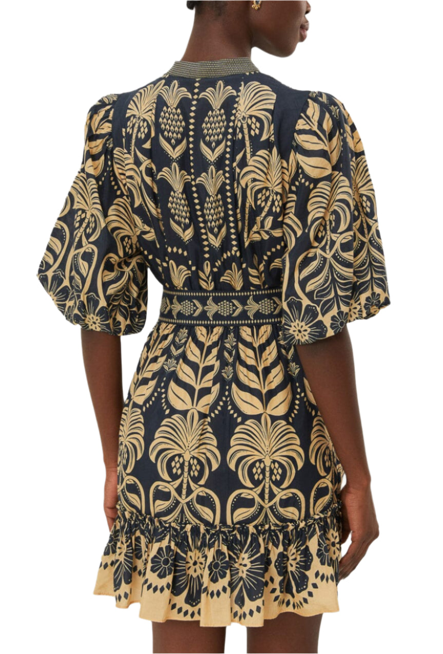 A person is seen from behind wearing the Farm Rio Ainika Tropical Splendor Blue Mini Dress, featuring puffed sleeves, a ruffled hem, and tropical patterns.