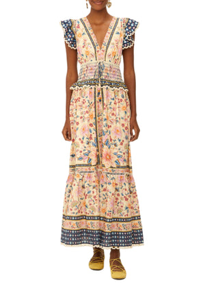 A woman in the Farm Rio Superbloom Tapestry Cream Maxi Dress—a sleeveless, floral maxi with V-neckline, ruffled shoulders, and tiered skirt—paired with yellow flats.