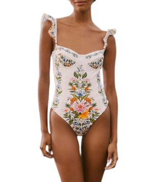 A woman wears the Farm Rio Sweet Bloom Bouquet One Piece, featuring an off-white base, colorful floral embroidery, ruffled shoulder straps, and a flattering sweetheart neckline.