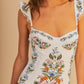 A woman wearing the Farm Rio Sweet Bloom Bouquet One Piece, an off-white swimsuit with vibrant floral prints, ruffled shoulder straps, and a flattering sweetheart neckline.