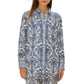 A woman wears the Farm Rio Blue Tropical Cameo Off-White Pajama Shirt, a long-sleeve, button-up top with a blue and white floral print made from LENZING™ ECOVERO™, standing against a plain white background.