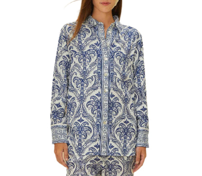 A woman wears the Farm Rio Blue Tropical Cameo Off-White Pajama Shirt, a long-sleeve, button-up top with a blue and white floral print made from LENZING™ ECOVERO™, standing against a plain white background.