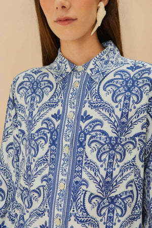 A woman wears the Farm Rio Blue Tropical Cameo Off-White Pajama Shirt, featuring an intricate floral pattern and eco-friendly LENZING™ ECOVERO™, paired with a large off-white earring.