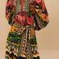 A person wearing Farm Rio's Coconut Tree Flow Dress with unique prints, puffed sleeves, and a V-neck collar stands against a neutral background.
