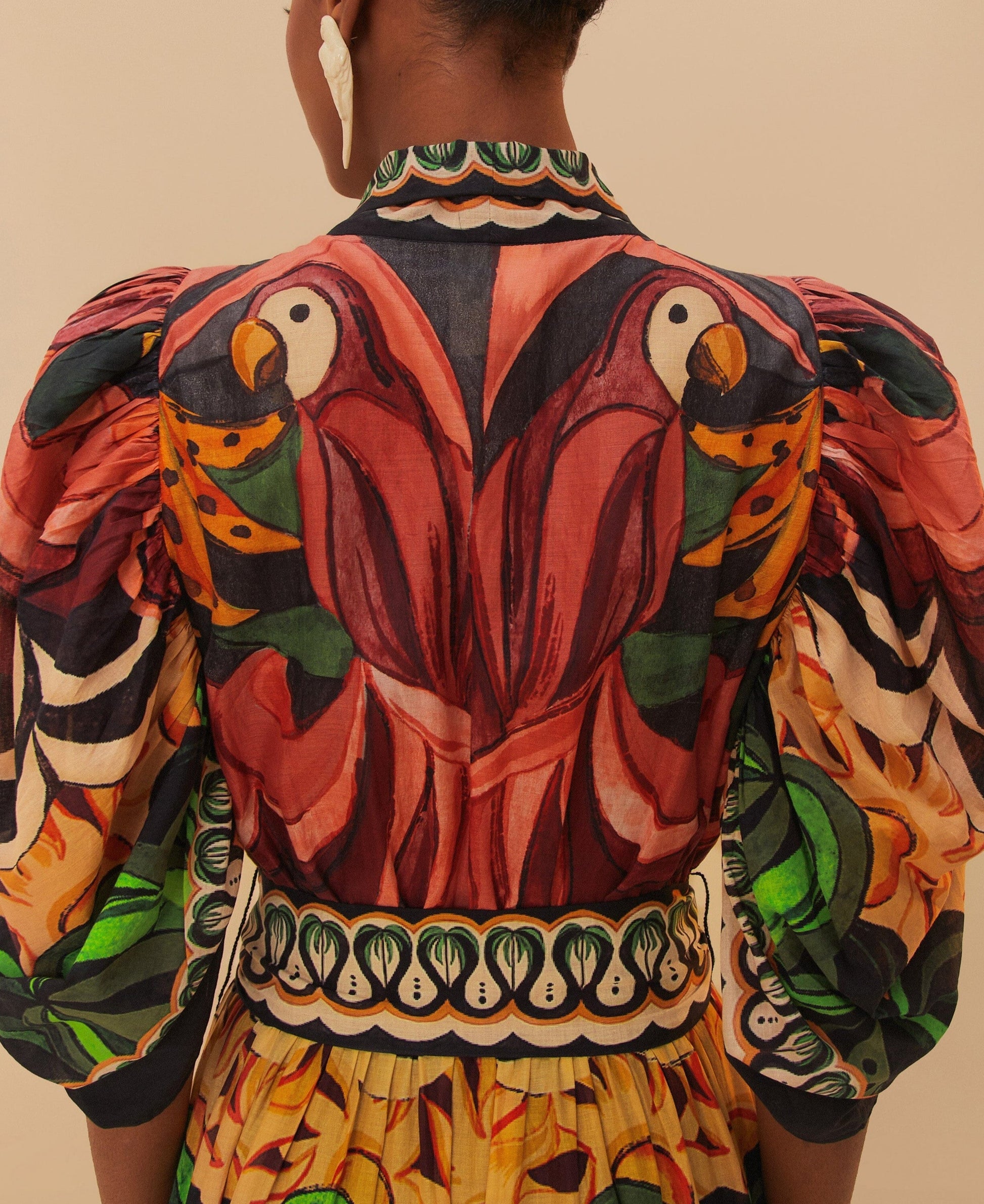 A person photographed from behind wears the Farm Rio Coconut Tree Flow Dress, featuring puffed sleeves and unique tropical patterns with a colorful parrot print on the back.