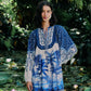 A woman stands by a pond with lily pads, wearing the Farm Rio Palm Tree Beach Off-White Mini Dress, featuring long sleeves and a vibrant tropical pattern that embodies lush, exotic style.