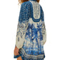 A woman showcases the Palm Tree Beach Off-White Mini Dress by Farm Rio—crafted from eco-responsible fibers, this loose blue and white long-sleeve piece features a vibrant palm tree print, radiating effortless tropical style from the back.