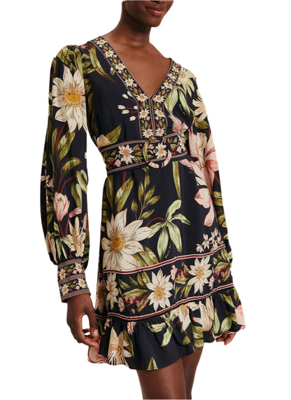 Person wearing a Farm Rio Surreal Flowers Black Long Sleeve Mini Dress, featuring a floral pattern with puffed sleeves, a V-neck, and ruffled hem.