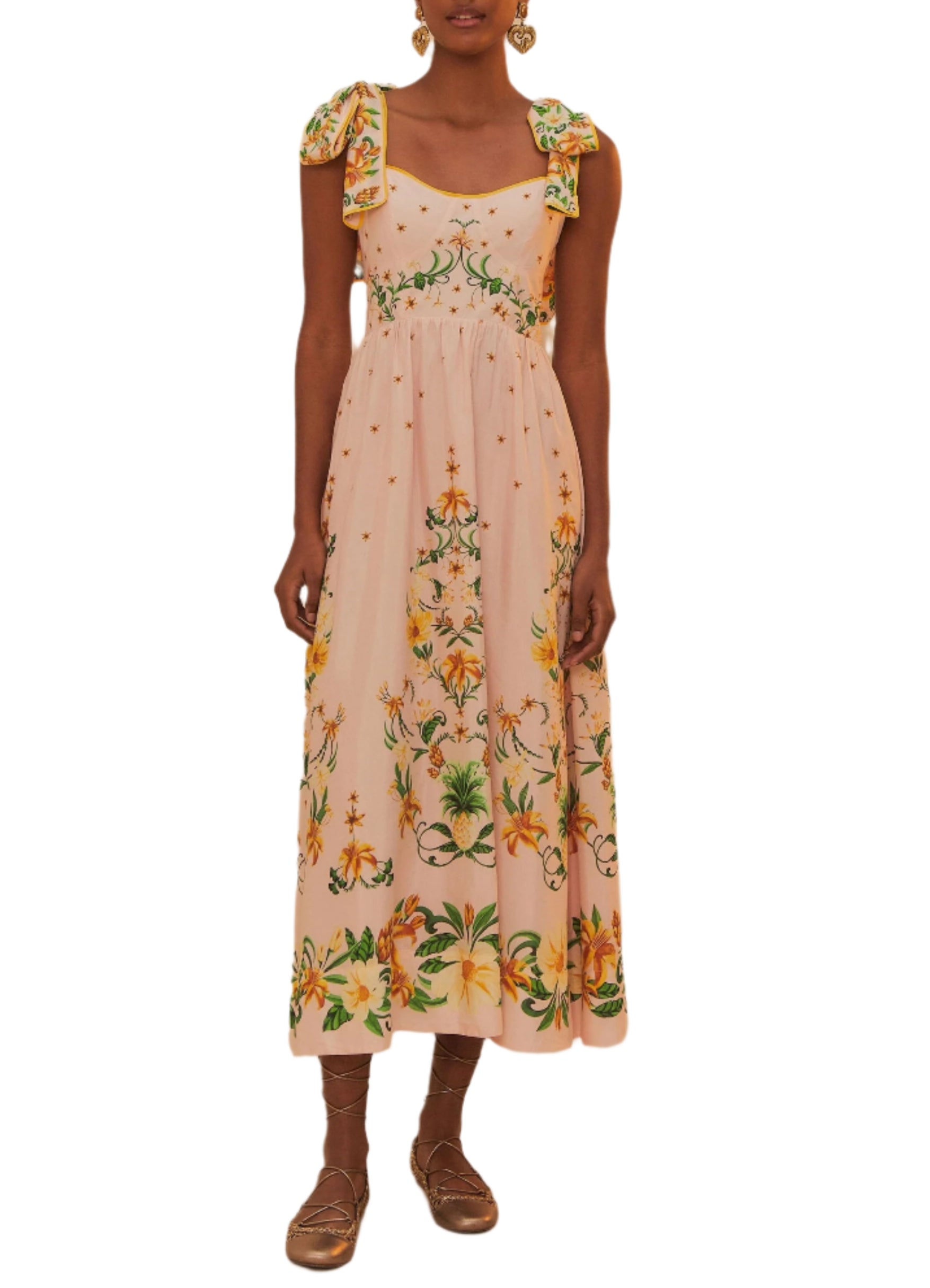 A woman wears the Farm Rio Botanical Beauty Shoulder Bow Midi Dress—an ankle-length, floral dress with bow-tied shoulder straps—and brown flat shoes.