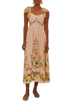 A woman wears the Farm Rio Botanical Beauty Shoulder Bow Midi Dress—an ankle-length, floral dress with bow-tied shoulder straps—and brown flat shoes.
