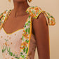 A woman in the Farm Rio Botanical Beauty Shoulder Bow Midi Dress, with botanical prints and shoulder bows, accessorizes with gold heart-shaped earrings.