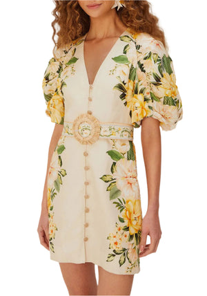 A woman wears the Farm Rio Garden Cascade Sand Mini Dress, featuring a cream floral pattern, puffed sleeves, deep V-neck, front buttons, and a wide belted waist. Made from Euroflax premium linen for chic comfort.