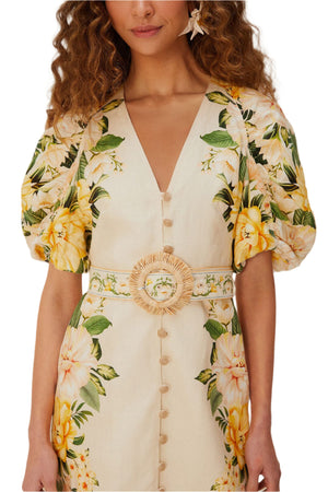 A woman wears the Farm Rio Garden Cascade Sand Mini Dress featuring a cream and yellow floral print, puffed sleeves, deep V-neckline, button front, and a matching belt with circular buckle.