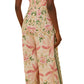 A woman wearing the Farm Rio Palm Dream Off White Jumpsuit, a sleeveless, wide-leg style with pink and green tropical patterns, photographed from the back.