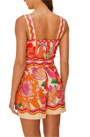 A woman is seen from the back wearing the Farm Rio Spring Affair Beige Romper, a sleeveless, belted LENZING™ ECOVERO™ piece with an orange, pink, and red floral print.