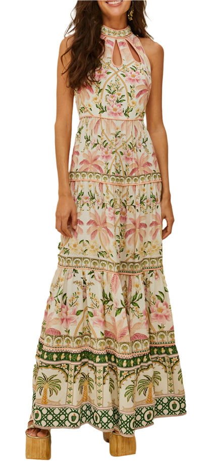 A woman wears the Farm Rio Palm Dream Off White Maxi Dress, featuring a sleeveless floral print, halter neckline, and tiered skirt, standing with her arms relaxed at her sides.