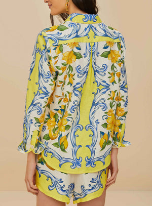A woman is seen from behind wearing the Farm Rio Sicily Scarf Off White Shirt, a matching long-sleeve top and shorts set with bright yellow florals and blue scrolls on white, radiating tropical elegance.