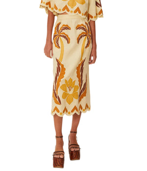 Someone wearing Farm Rio’s Summer Cutwork Sand Skirt, a premium linen piece with brown and yellow palm tree and floral patterns, paired with platform sandals.