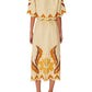 A woman is shown from the back wearing Farm Rio’s Summer Cutwork Sand Skirt, featuring short sleeves, yellow and brown floral appliqué, cutwork patterns, scalloped edges, and brown platform sandals.