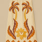 The Summer Cutwork Sand Skirt by Farm Rio features brown and yellow palm tree and floral appliqué with large leaves and a scalloped hem, inspired by FARM Rio’s signature cutwork patterns on a neutral beige background.
