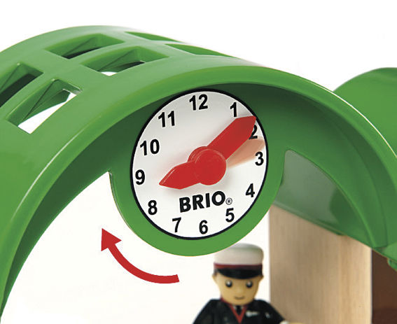 A clock with a red hand and a green object with a BRIO World railway set.