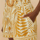 Wearing FARM Rio's Lace Nature Off-White Shorts, made from eco-responsible fibers, styled with a wide belt and a white blouse with lace sleeves that feature FARM Rio's iconic leafy patterns.