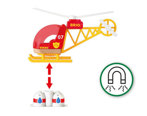 A red and yellow Brio World Firefighter Helicopter labeled "07 BRIO" hovers above two white objects with blue and red drops, indicating magnetic pickup. A magnet symbol is shown on the right, suggesting the pilot can use it to assist in water supply operations.