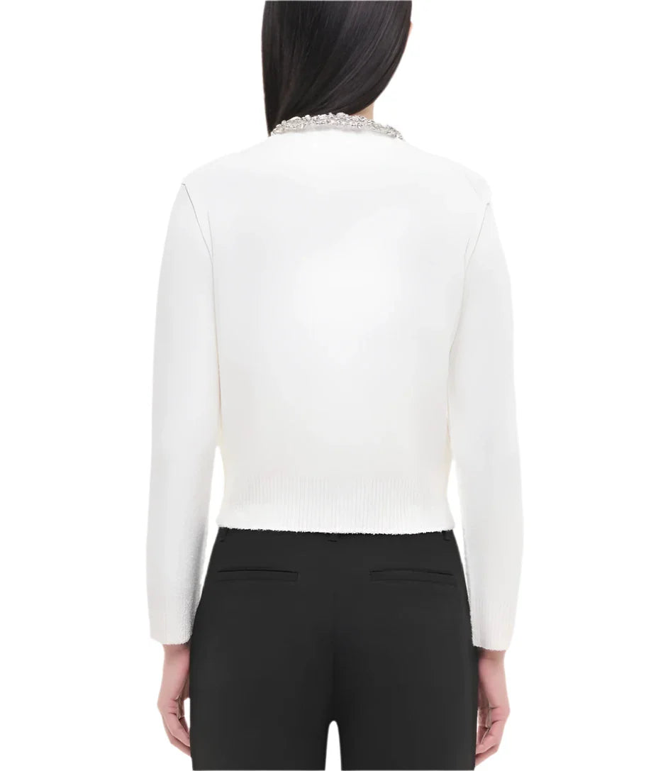 A person with long dark hair is seen from behind wearing the flattering Simkhai Lieghton Boucle Cardigan, a white sweater with a pearl collar, paired with black pants.