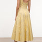 A woman stands on a light brown floor wearing the Staud Wells Monday Stripe Lobster Dress—a yellow, sleeveless, mid-length fitted waist dress with black vertical stripes—and black slide sandals.