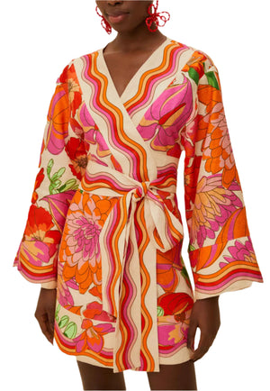 A person wearing the Farm Rio Spring Affair Beige Mini Dress, a long-sleeve, wrap-style mini dress with bold floral and wavy stripe patterns in pink, orange, red, and cream Euroflax Premium Linen.